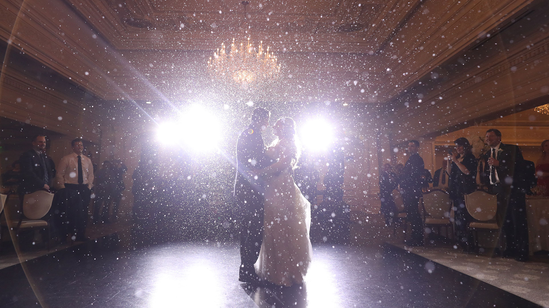 bride and groom dance with spotlights behind them and fake snow falling in the room